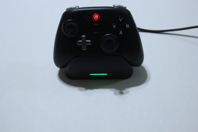 Black game controller resting on a charging dock with a green status light.