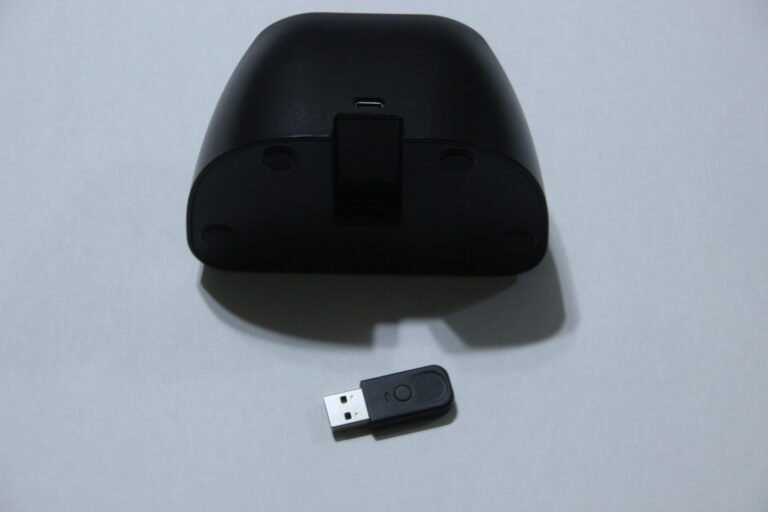 Underside of a black wireless mouse with a USB receiver lying on a gray surface.