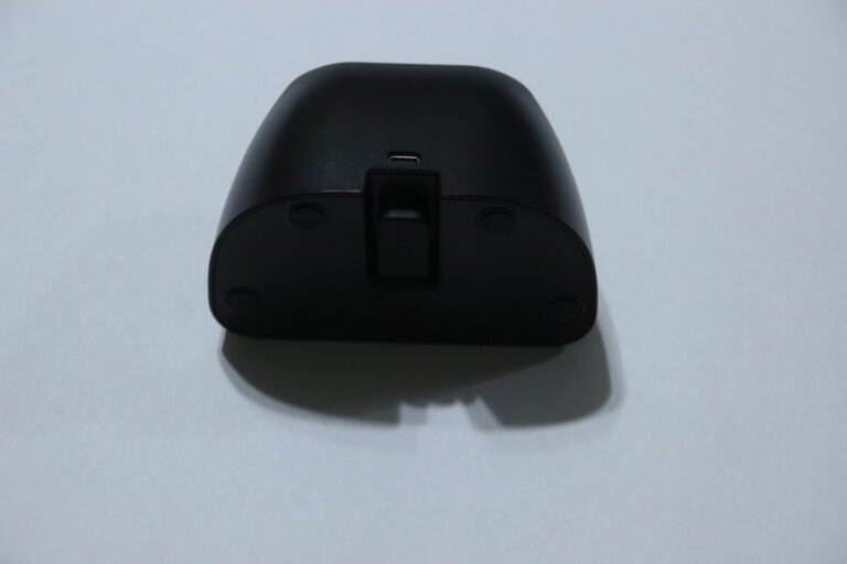 Bottom view of a black device with a small USB-C port in the center and four circular feet on a white surface.