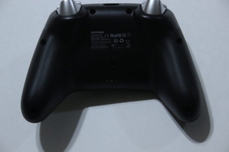 Back view of black game controller with textured grips and central label plate showing certifications and model info