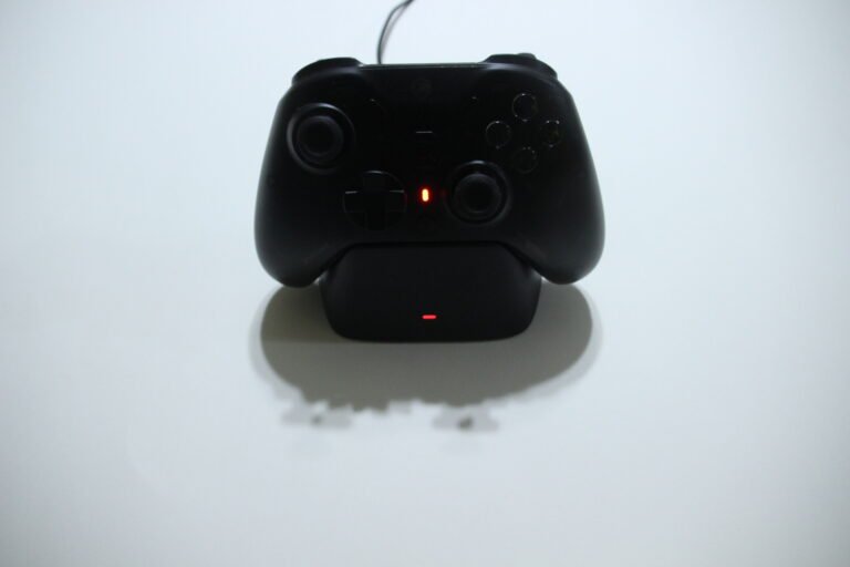 Black game controller resting on a charging dock with a red indicator light