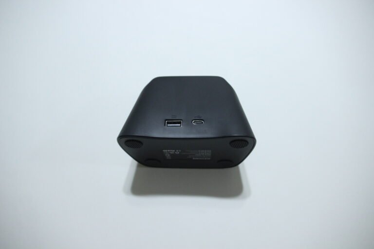 Bottom view of a black cube-shaped speaker showing a USB-A port and a USB-C port on a white surface