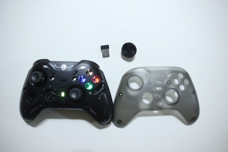 Two game controllers on a white surface, with a small USB dongle and a tiny thumbstick cap above them.