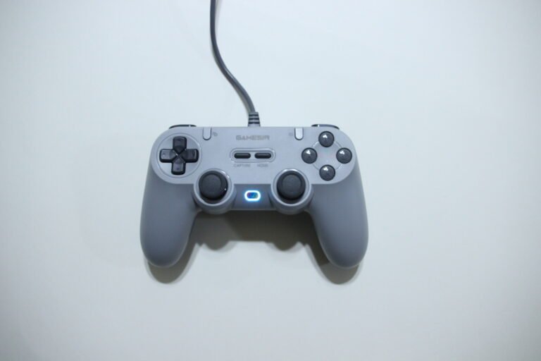 Front view of a gray wired game controller with two analog sticks, D-pad, and buttons on a white background, highlighting the cable leading up from it.