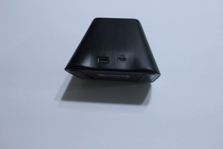 Black wall charger brick with two ports (USB-A on left, USB‑C on right) facing the camera on a white surface.