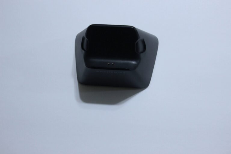 Black charging dock resting on a square base, with two small gold charging contacts visible on the front edge.