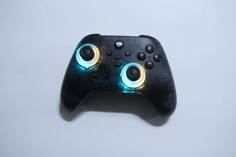 Top-down view of a black game controller with blue glowing rings around the analog sticks on a white background.