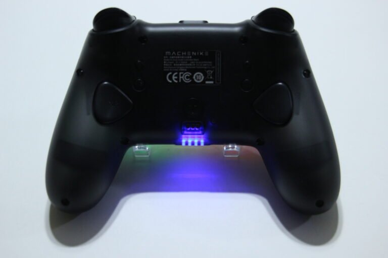 Back view of a black game controller with a blue LED glow emanating from the center connector area.