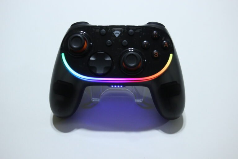 Black wireless game controller with RGB LED ring around front and blue glow underneath on a white surface.