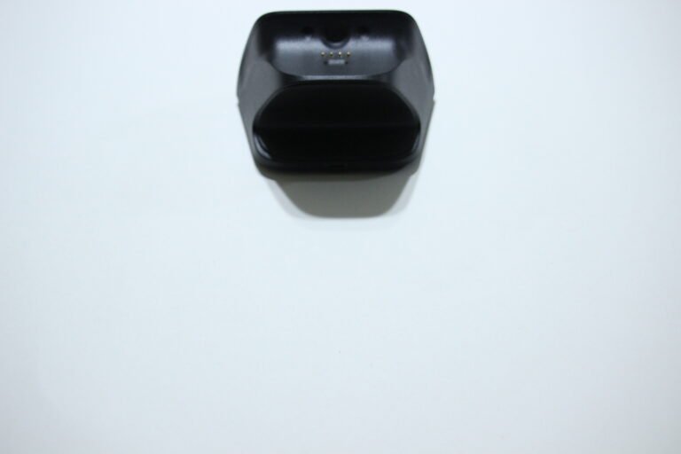 Overhead view of a black charging cradle with gold contact pins on a white surface, ready to dock a device.