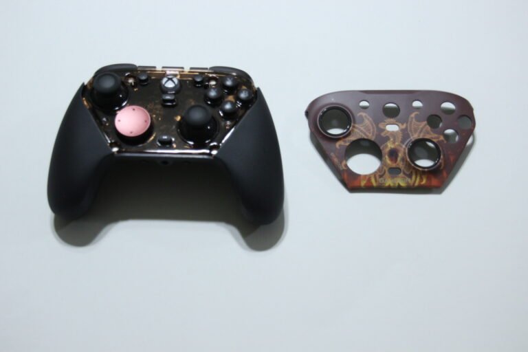 Two disassembled game controller shells on a white surface: a black left shell with a pink circular button and sticks, and a brown patterned right faceplate with multiple holes.