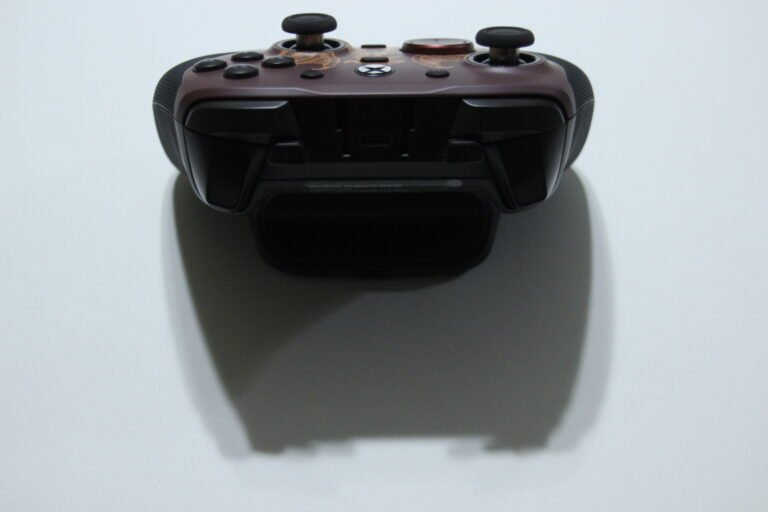 Top-down view of a brown game controller with two analog sticks, a D-pad, and multiple buttons on a white surface.