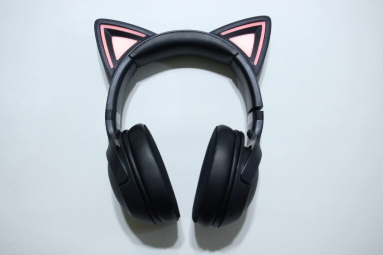 Black over-ear headphones with pink cat-ear tips on the headband on a pale surface.
