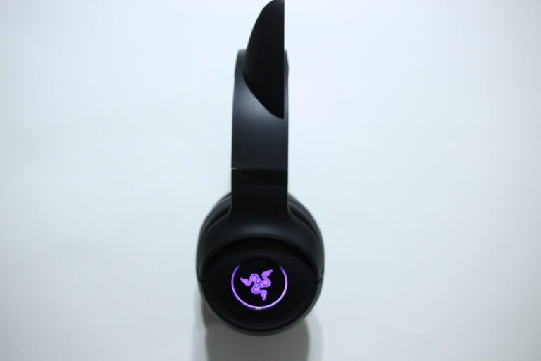 Top-down view of a black gaming headset with a purple glowing logo on the ear cup against a light background.